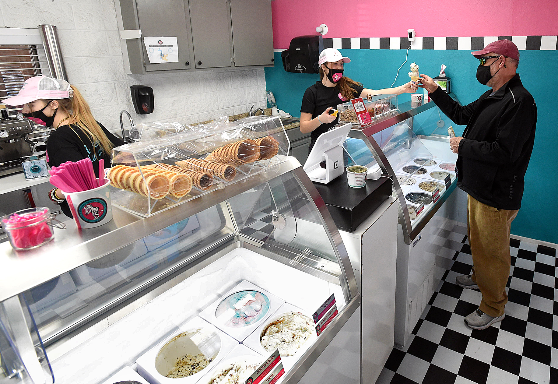 LOVELAND, CO - JANUARY 22, 2021:   Ariana Dodds, center right, hands and ice cream cone to customer Tom Buchanan, right, on Friday, Jan. 22, 2021, at her new ice cream shop, Ice Scream Ice Cream at 4221 W. Eisenhower Blvd. in the Former Esh's Grocery store building in west Loveland. Employee Cameo Blakeney, far left, prepares the rest of the order.    (Jenny Sparks/Loveland Reporter-Herald)